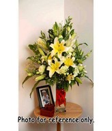 Creme lilies with white eustoma and yellow phoenix in long glass vase filled with vibrant red chilli